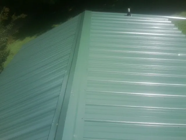 New green metal panels meeting at the ridge of a roof — Flat Roof Repair work by our crew in Berlin