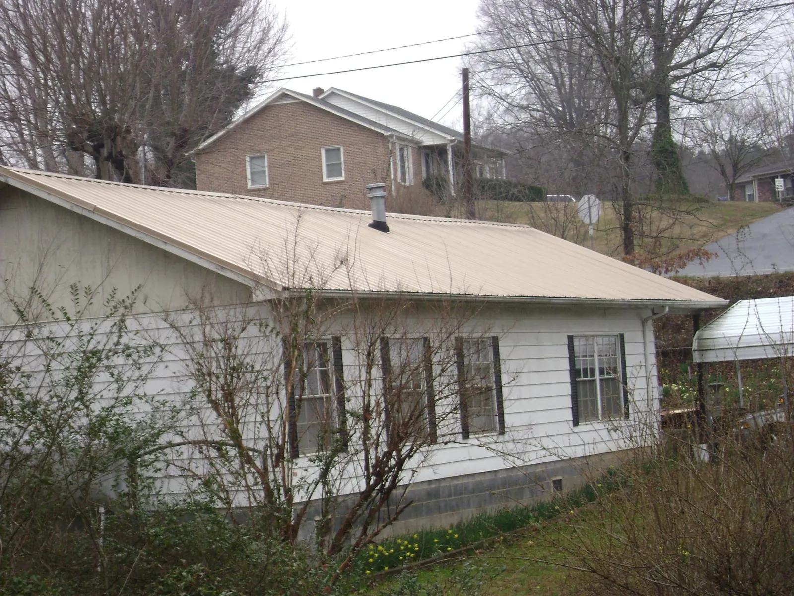 Tan metal roof on a white sided house set into a hillside — Commercial Roofing by Roofing Brothers in Berlin
